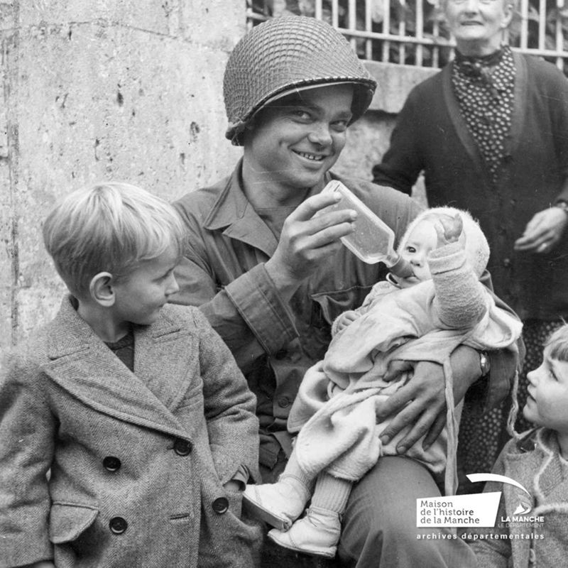 Un soldat américain donne à boire à un bébé, cliché publié dans "Yank" le 3 septembre 1944 (Archives de la Manche, fonds des photographies américaines, 13 Num 1329) 